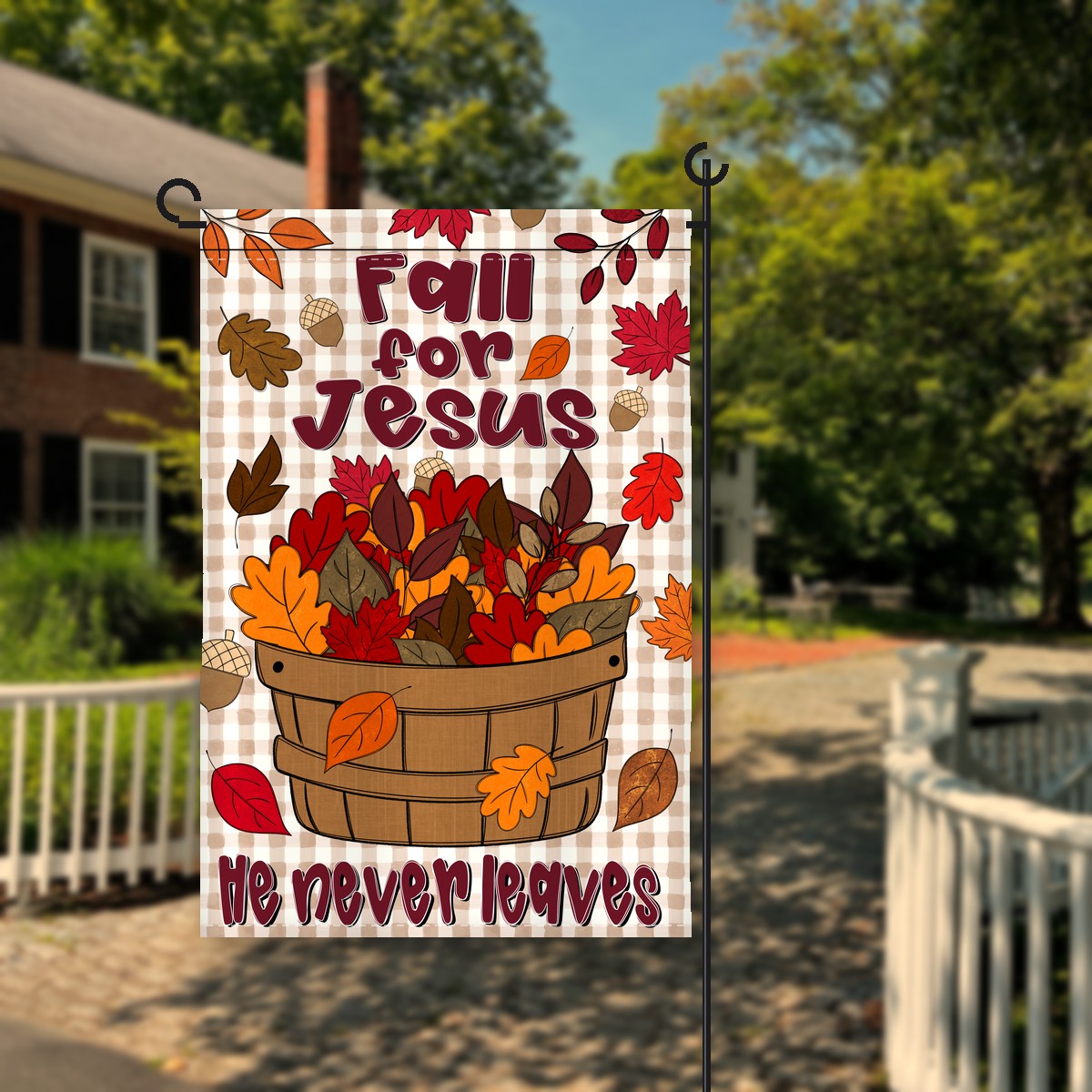Fall for Jesus garden flag with a bushel basket of red, orange and brown leaves on tan gingham and He never leaves, on a flag stand in a front yard, by Oyster Creek in Eden, NC